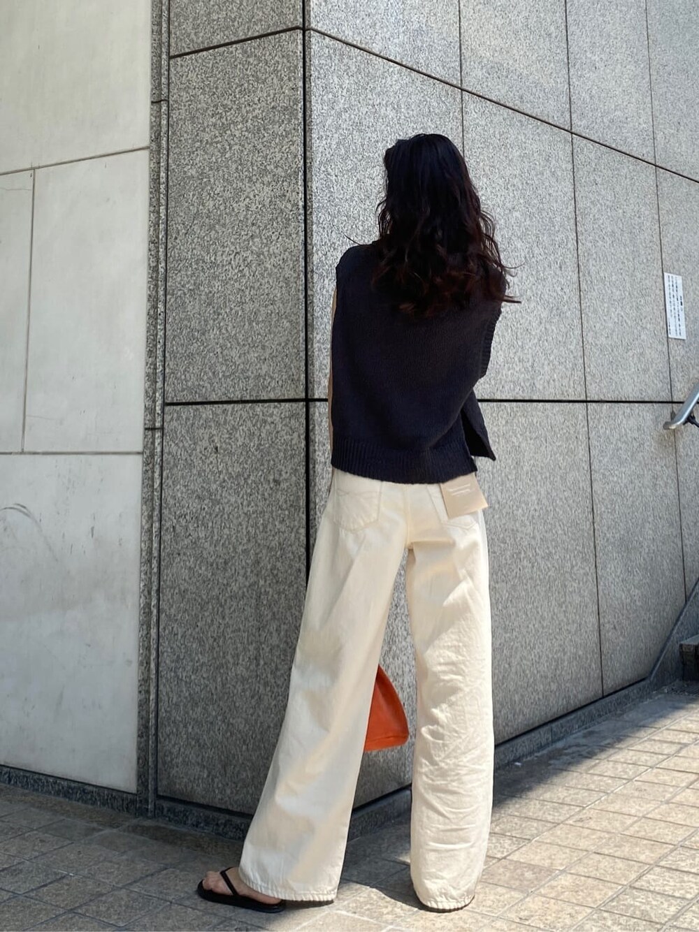 オレンジ系のハンドバッグ、ホワイト系のデニムパンツ、グレー系のベストを着用したレディースの春コーディネートの4枚目の写真