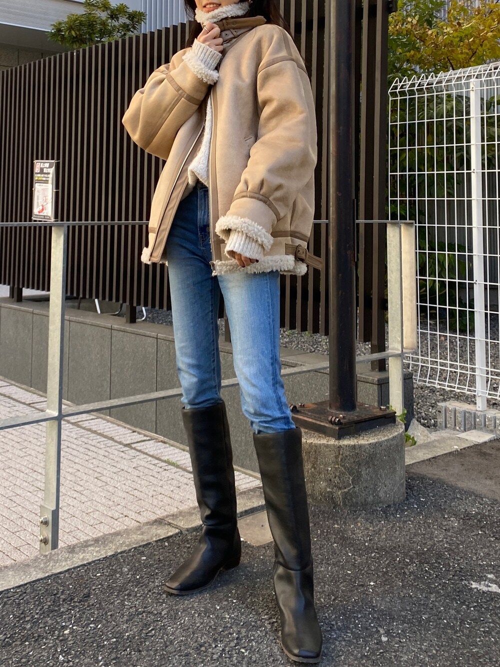 ベージュ系のムートンコート、ホワイト系のニット/セーター、ブルー系のデニムパンツを着用したレディースの冬コーディネートの2枚目の写真