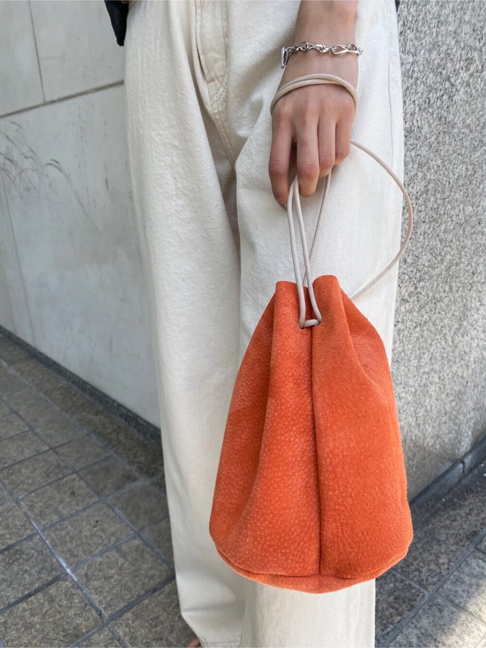 オレンジ系のハンドバッグ、ホワイト系のデニムパンツ、グレー系のベストを着用したレディースの春コーディネートの7枚目の写真