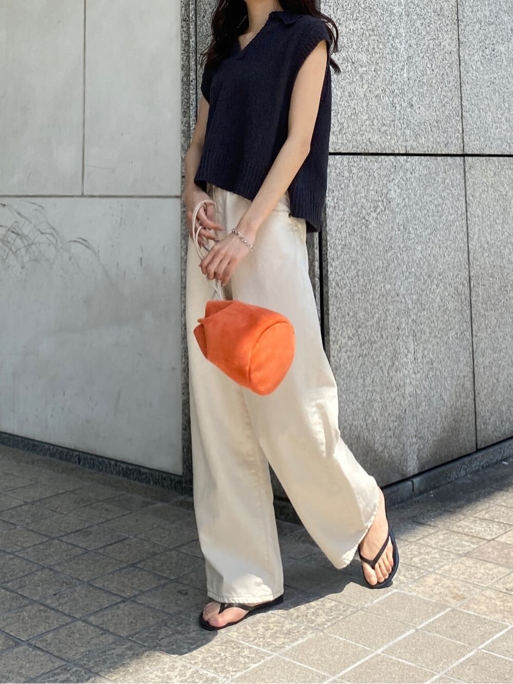 オレンジ系のハンドバッグ、ホワイト系のデニムパンツ、グレー系のベストを着用したレディースの春コーディネートの2枚目の写真