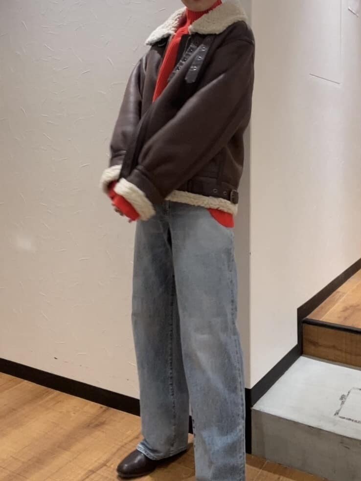 オレンジ系のニット/セーター、ブラウン系のムートンコート、ブルー系のデニムパンツを着用したレディースの秋コーディネートの2枚目の写真