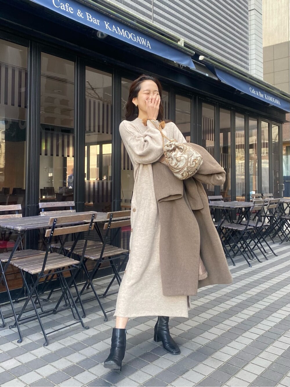 ベージュ系のチェスターコート、ホワイト系のハンドバッグ、グレー系のワンピースを着用したレディースの秋コーディネートの3枚目の写真