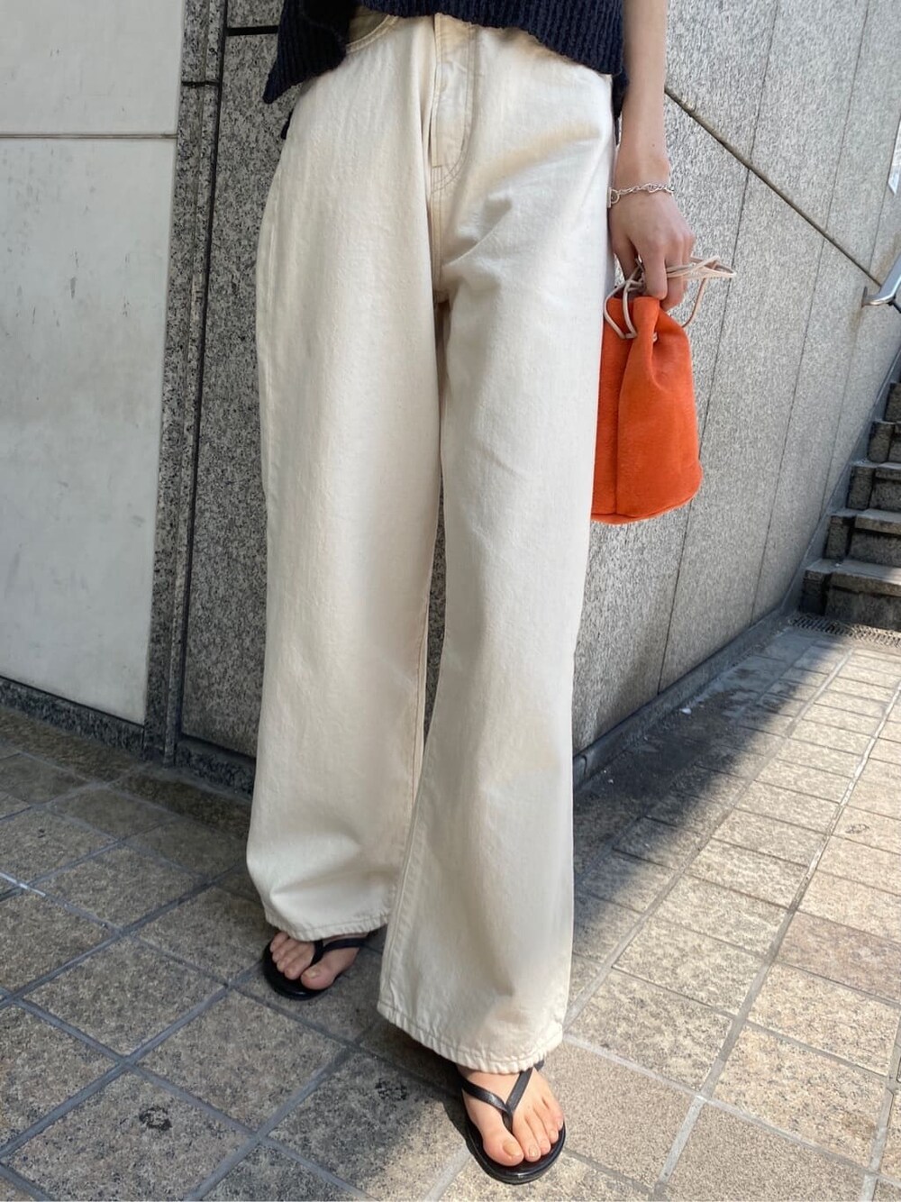 オレンジ系のハンドバッグ、ホワイト系のデニムパンツ、グレー系のベストを着用したレディースの春コーディネートの6枚目の写真