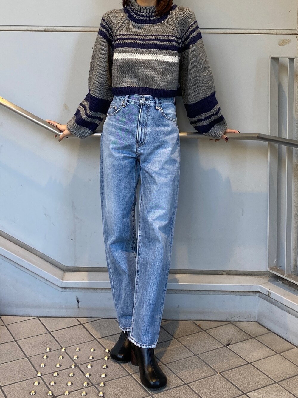 グレー系のニット/セーター、ブルー系のデニムパンツ、ブラック系のブーツを着用したレディースの秋コーディネートの2枚目の写真