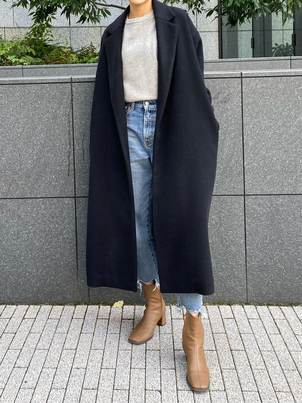 ブラック系のチェスターコート、ブルー系のデニムパンツ、グレー系のニット/セーターを着用したレディースの秋コーディネートの2枚目の写真