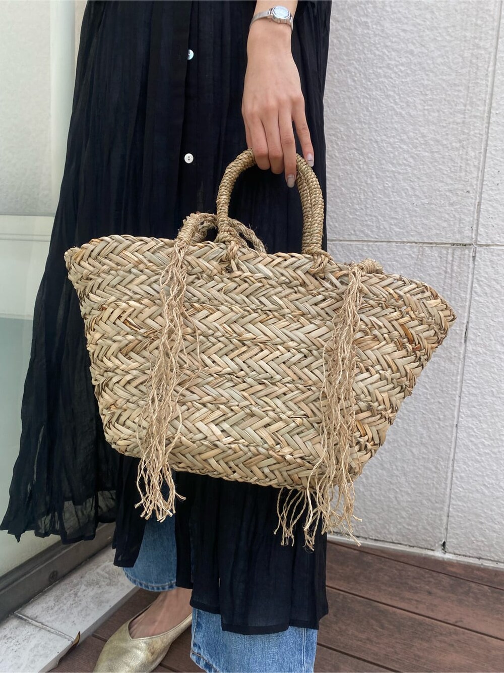 ブルー系のデニムパンツ、ブラック系のワンピース、ベージュ系のかごバッグを着用したレディースの春コーディネートの7枚目の写真