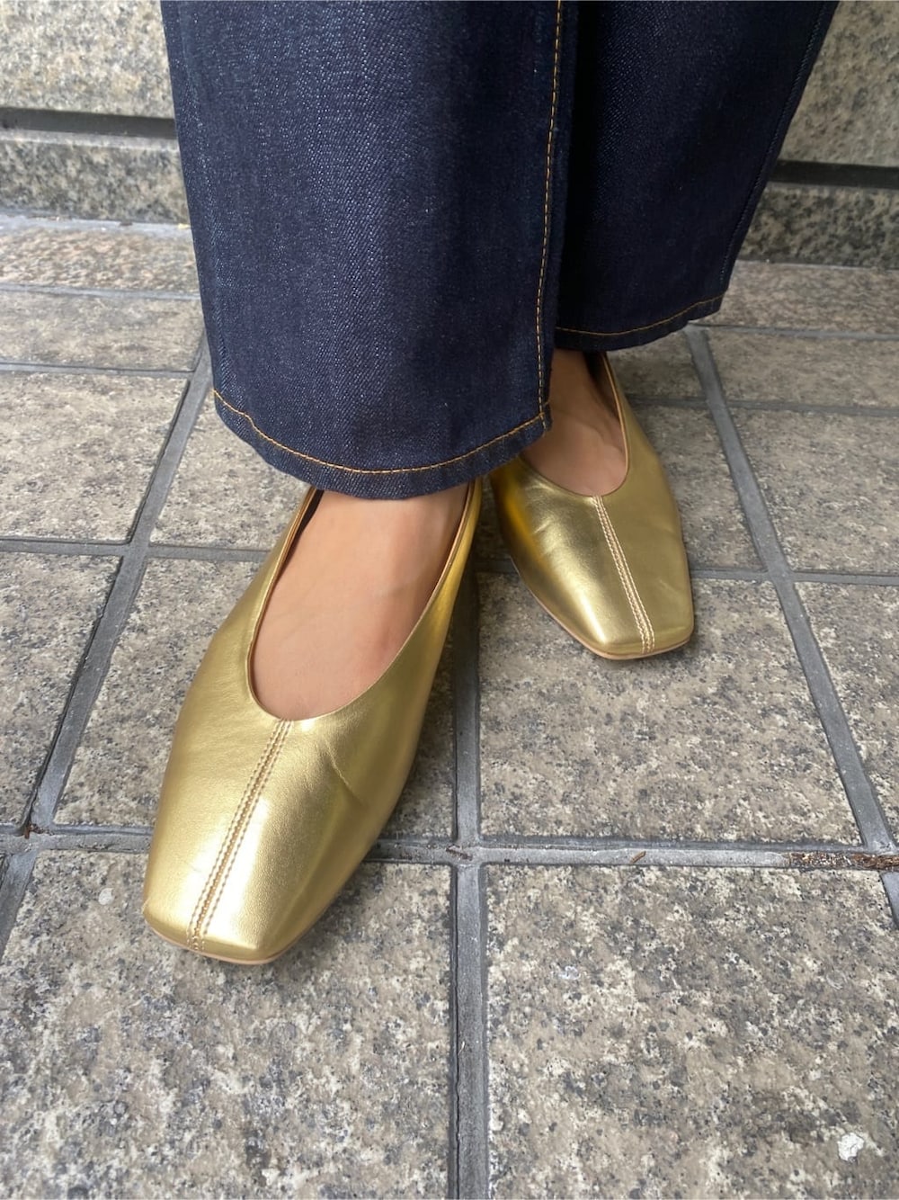 ゴールド系のパンプス、ブラック系のハンドバッグ、ブルー系のデニムパンツを着用したレディースの秋コーディネートの8枚目の写真