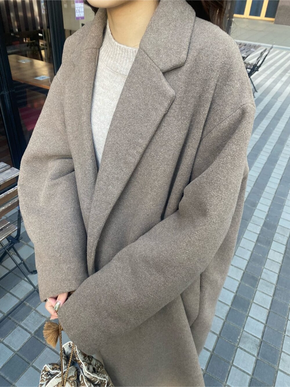 ベージュ系のチェスターコート、ホワイト系のハンドバッグ、グレー系のワンピースを着用したレディースの秋コーディネートの6枚目の写真