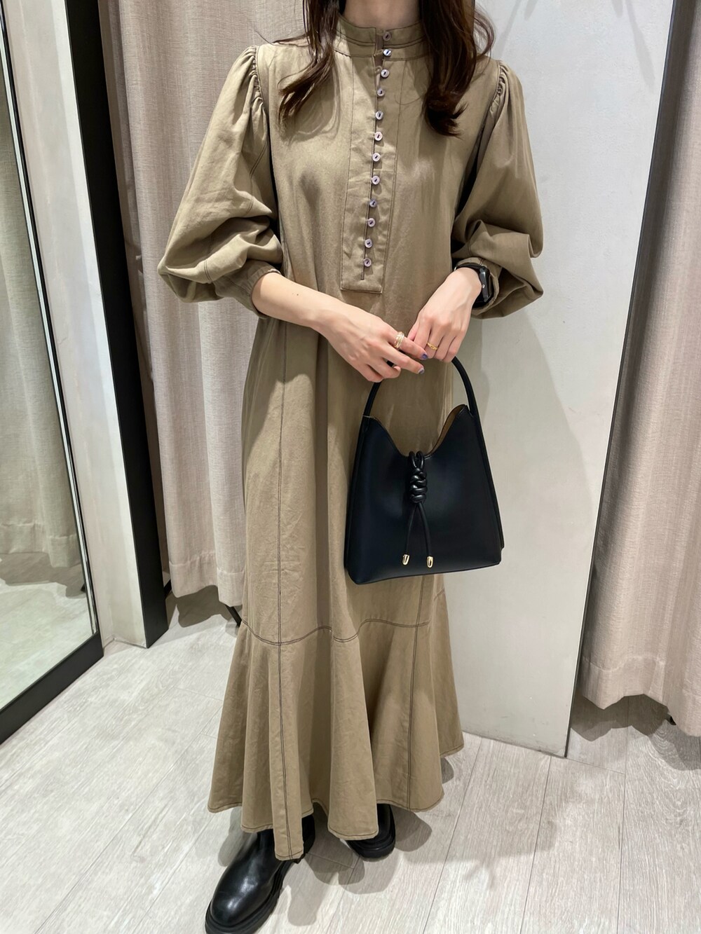 ブラック系のハンドバッグ、ベージュ系のワンピース、ブラック系のブーツを着用したレディースの秋コーディネートの2枚目の写真