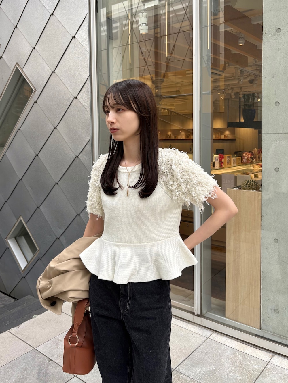 ブラック系のデニムパンツ、ホワイト系のニット/セーター、ベージュ系のトレンチコートを着用したレディースの春コーディネートの2枚目の写真