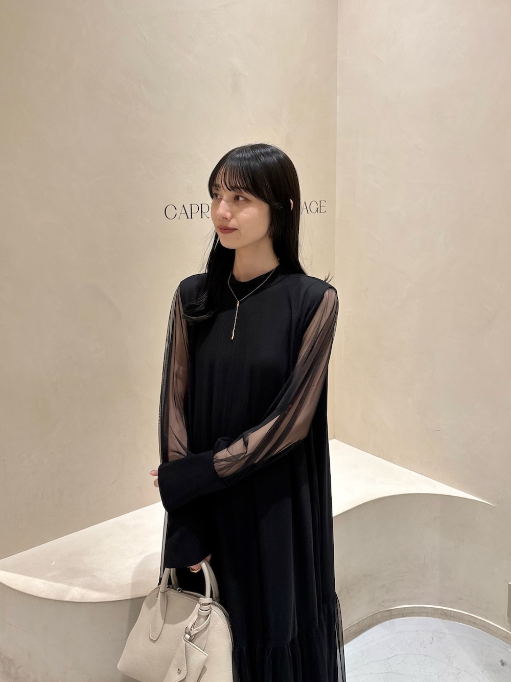 ブラック系のワンピース、ホワイト系のショルダーバッグ、ブラック系のパンプスを着用したレディースの春コーディネートの2枚目の写真