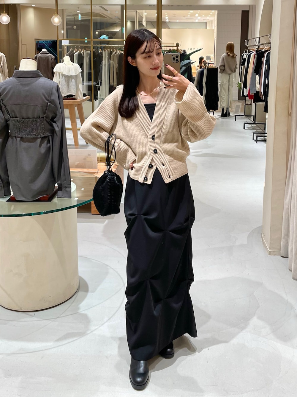 ベージュ系のカーディガン/ボレロ、ブラック系のスカート、ブラック系のブーツを着用したレディースの秋コーディネートの2枚目の写真