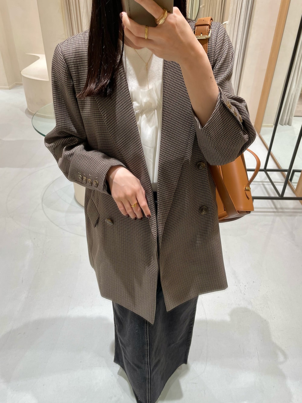 ブラウン系のテーラードジャケット、ブラック系のデニムスカート、ホワイト系のニット/セーターを着用したレディースの秋コーディネートの2枚目の写真