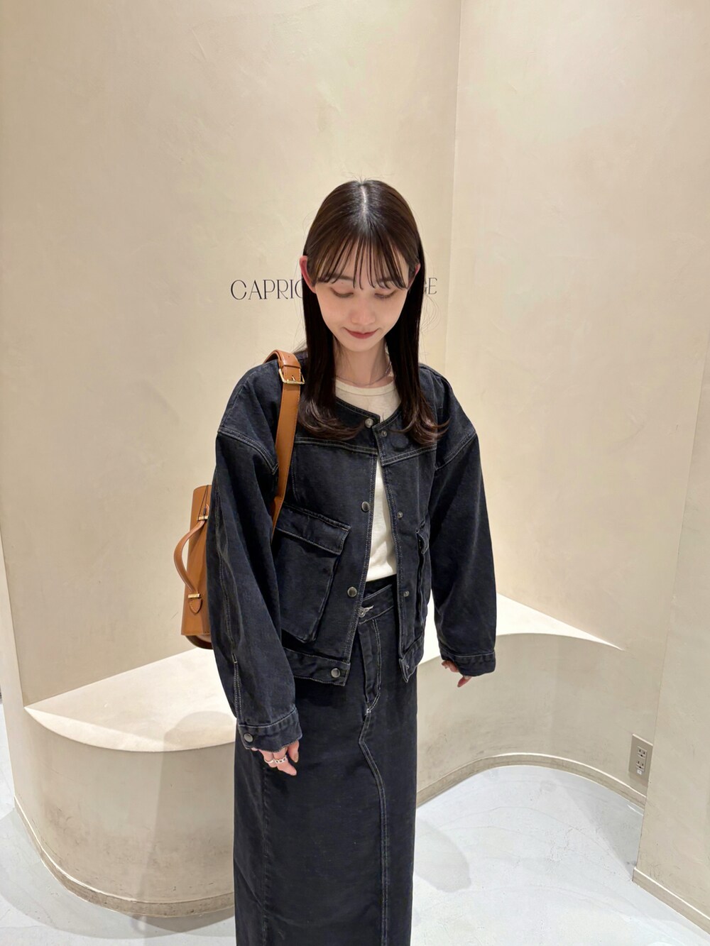 ブラック系のデニムスカート、ブラック系のデニムジャケット、ベージュ系のTシャツ/カットソーを着用したレディースの冬コーディネートの2枚目の写真