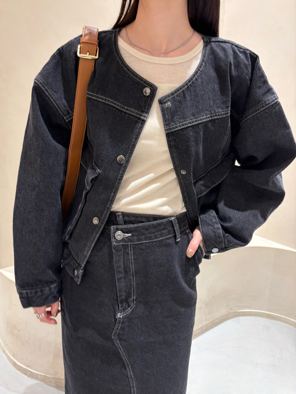 ブラック系のデニムスカート、ブラック系のデニムジャケット、ベージュ系のTシャツ/カットソーを着用したレディースの冬コーディネートの3枚目の写真