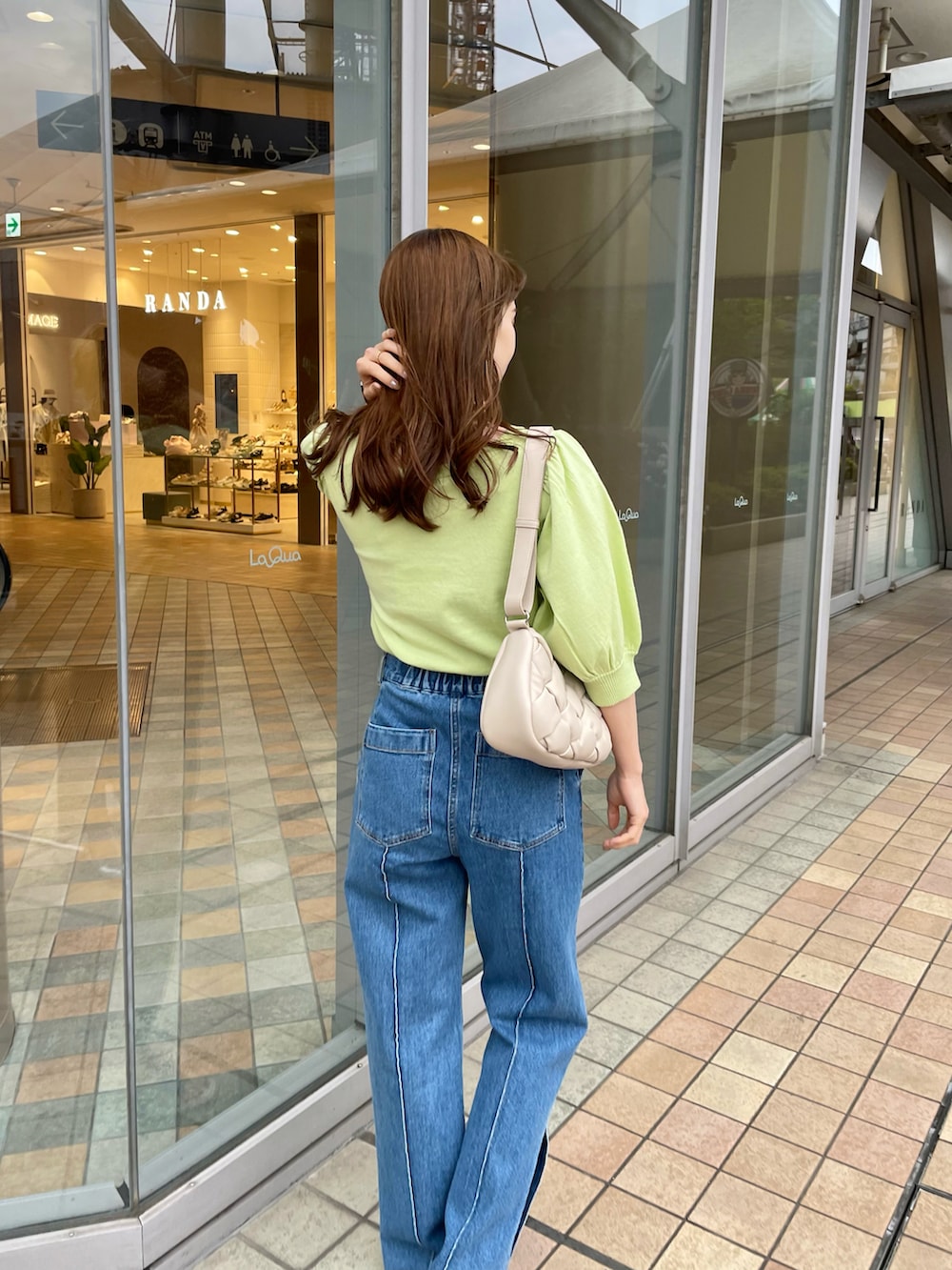 ブルー系のデニムパンツ、グリーン系のニット/セーター、ホワイト系のサンダルを着用したレディースの春コーディネートの3枚目の写真