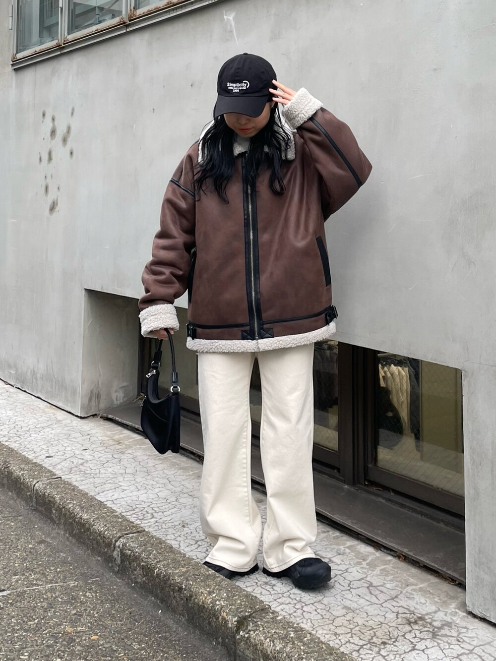 ブラック系のムートンコート、ホワイト系のデニムパンツ、ブラック系のハンドバッグを着用したレディースの冬コーディネートの2枚目の写真