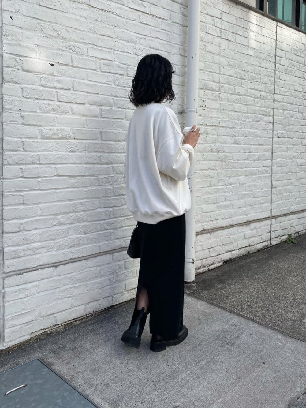 ブラック系のスカート、ホワイト系のスウェット、ブラック系のブーツを着用したレディースの冬コーディネートの3枚目の写真