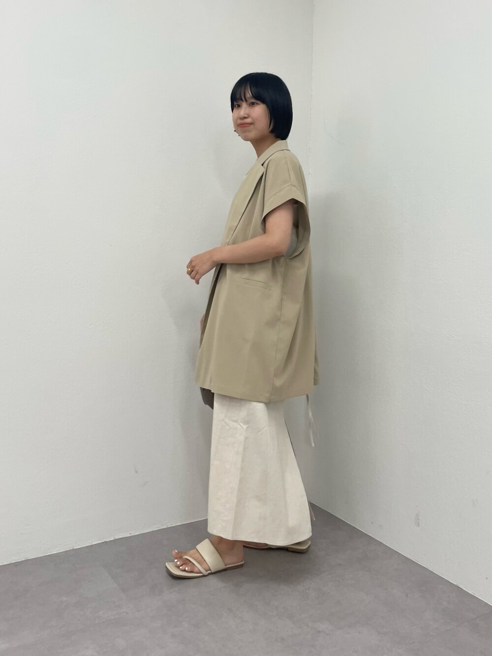 ベージュ系のベスト、ホワイト系のワンピース、ホワイト系のサンダルを着用したレディースの夏コーディネートの2枚目の写真