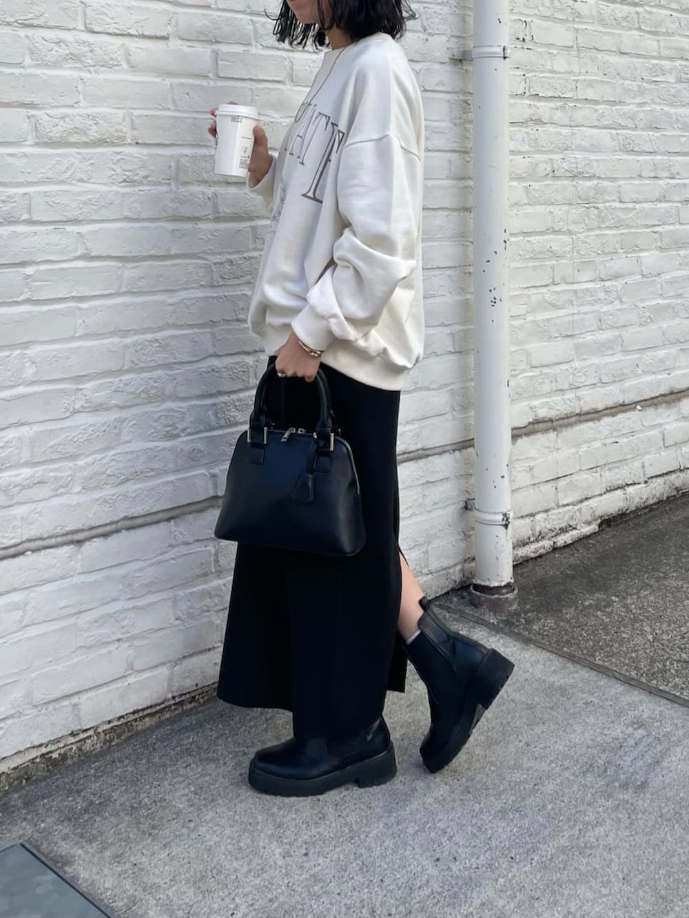 ブラック系のスカート、ホワイト系のスウェット、ブラック系のブーツを着用したレディースの冬コーディネートの2枚目の写真
