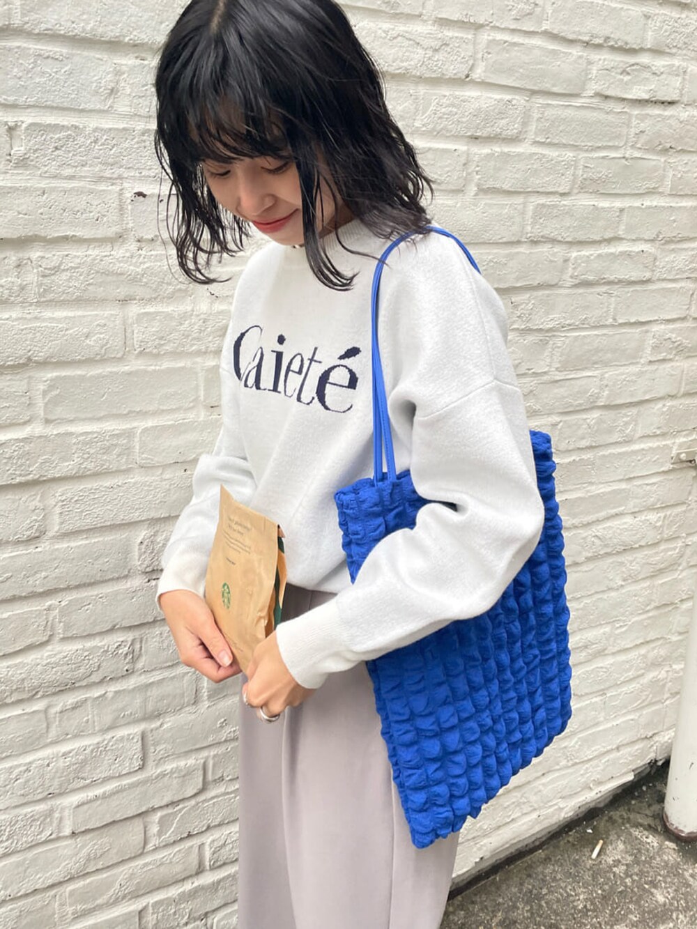 グレー系のその他パンツ、ホワイト系のニット/セーター、ブルー系のトートバッグを着用したレディースの冬コーディネートの3枚目の写真