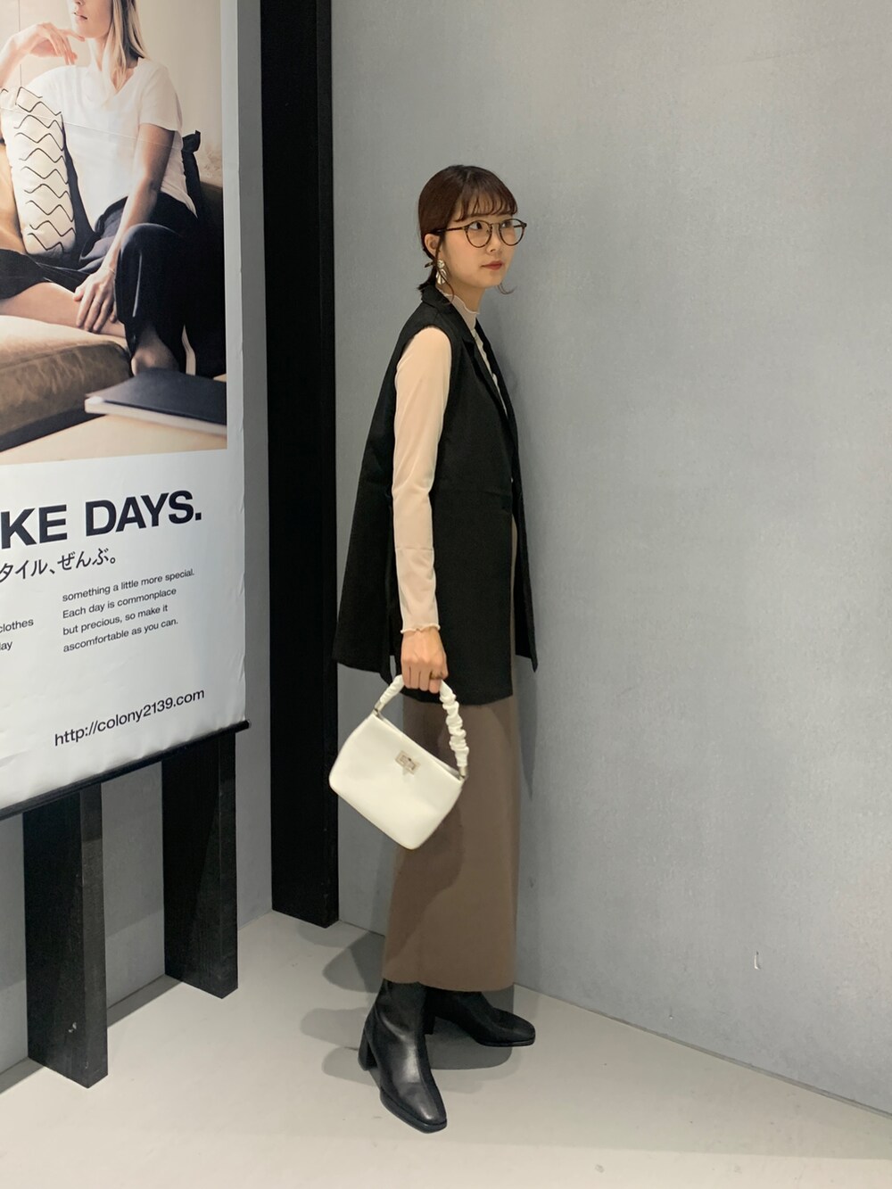 ホワイト系のハンドバッグ、ブラウン系のスカート、ブラック系のブーツを着用したレディースの秋コーディネートの2枚目の写真