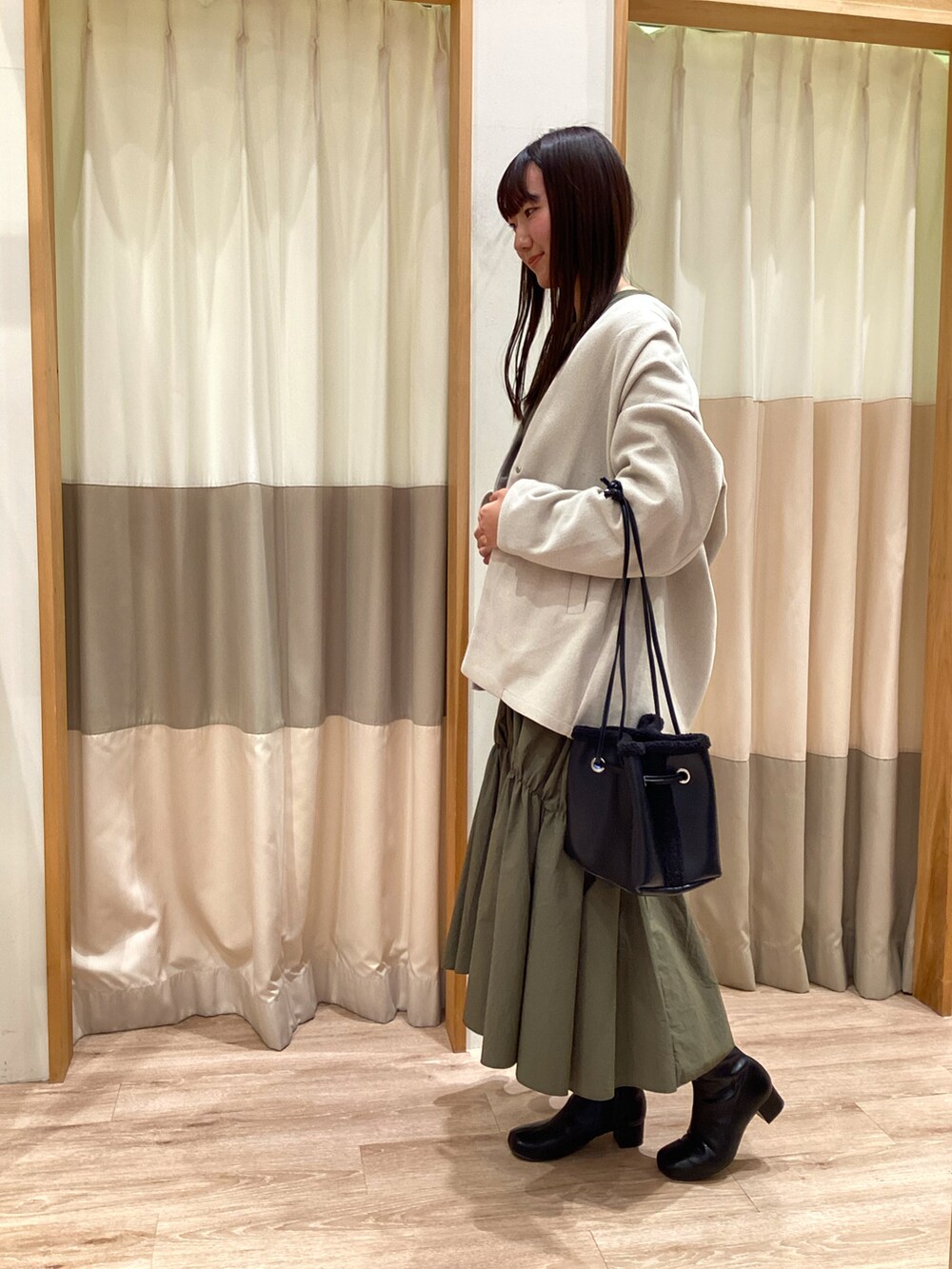 グリーン系のワンピース、ブラック系のハンドバッグ、ブラック系のブーツを着用したレディースの秋コーディネートの2枚目の写真