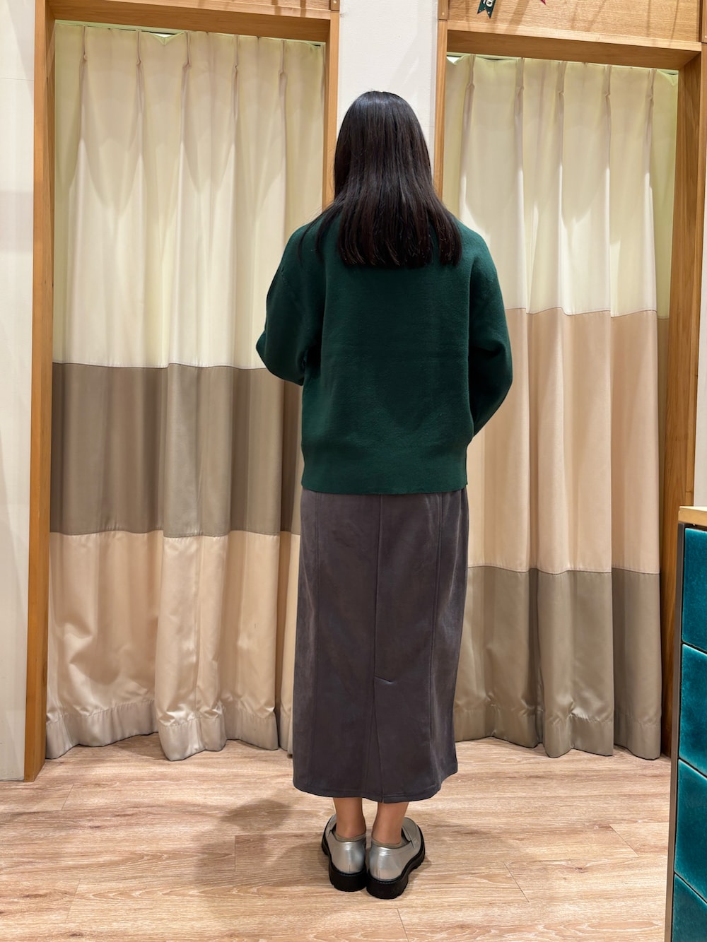 グリーン系のニット/セーター、グレー系のスカート、シルバー系のハンドバッグを着用したレディースの冬コーディネートの2枚目の写真