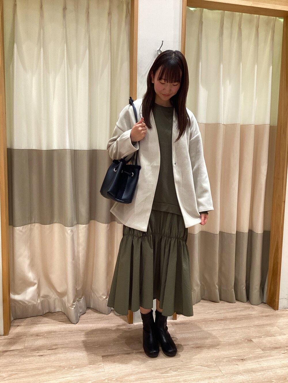 グリーン系のワンピース、ブラック系のハンドバッグ、ブラック系のブーツを着用したレディースの秋コーディネートの3枚目の写真