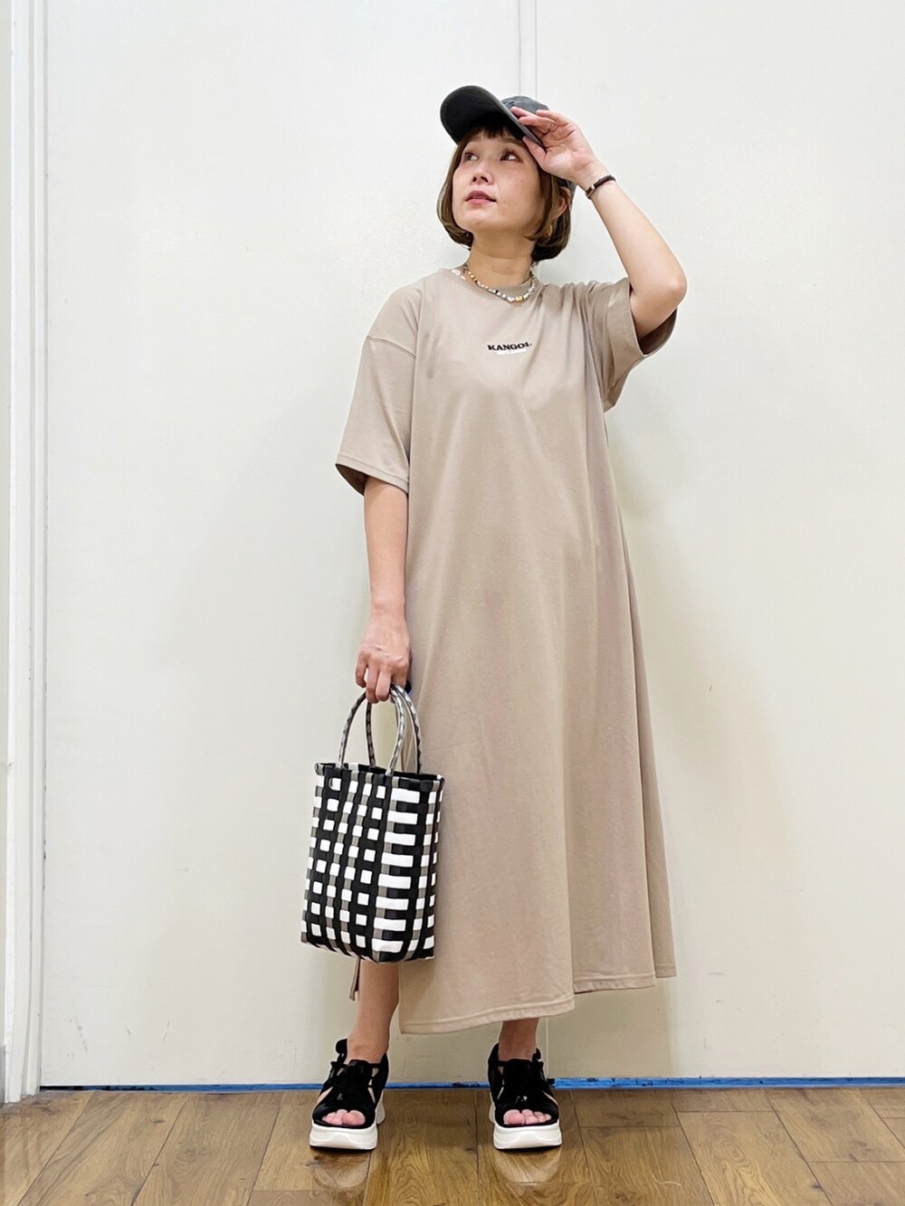 ベージュ系のワンピース、ブラック系のサンダル、ブラック系のかごバッグを着用したレディースの夏コーディネートの2枚目の写真
