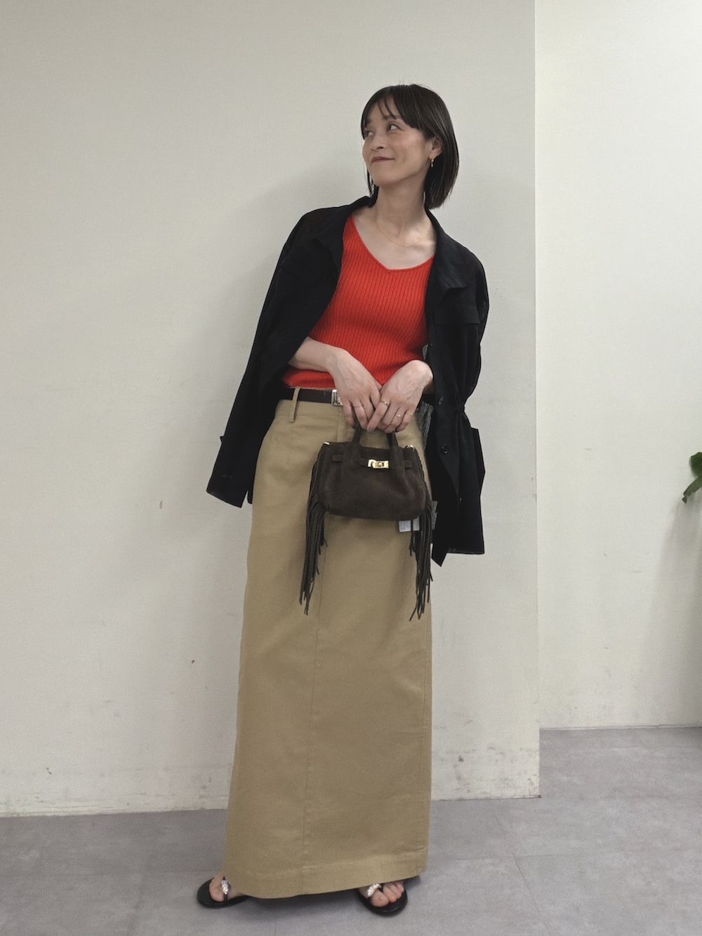 ブラック系のベスト、オレンジ系のニット/セーター、ベージュ系のスカートを着用したレディースの春コーディネートの4枚目の写真