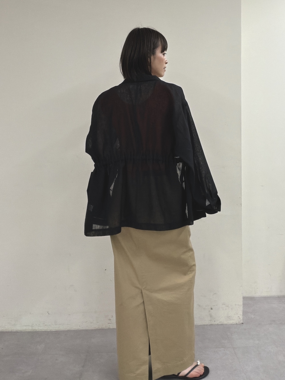 ブラック系のベスト、オレンジ系のニット/セーター、ベージュ系のスカートを着用したレディースの春コーディネートの3枚目の写真