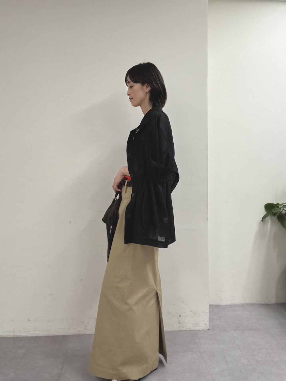 ブラック系のベスト、オレンジ系のニット/セーター、ベージュ系のスカートを着用したレディースの春コーディネートの2枚目の写真