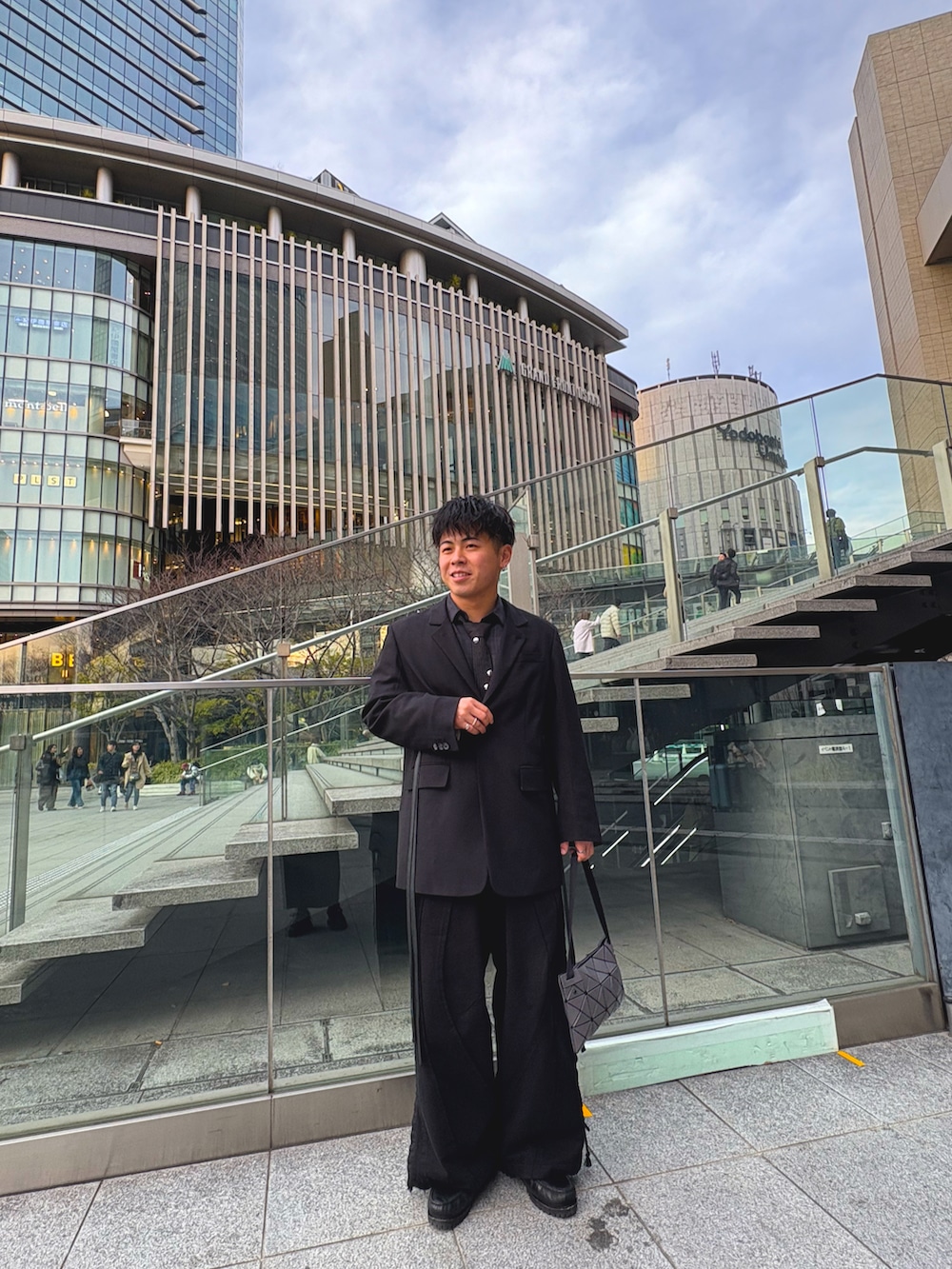 グレー系のバッグ、ブラック系のデニムパンツ、ブラック系のテーラードジャケットを着用したメンズの春コーディネートの2枚目の写真