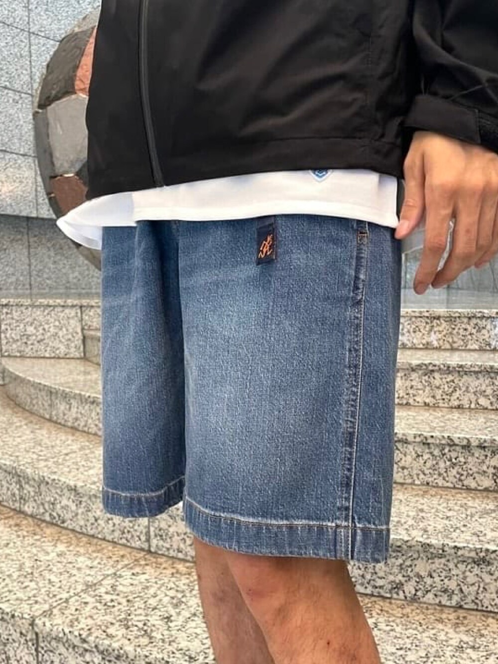 ブラック系のブルゾン、ホワイト系のTシャツ/カットソー、ブルー系のデニムパンツを着用したメンズの春コーディネートの4枚目の写真