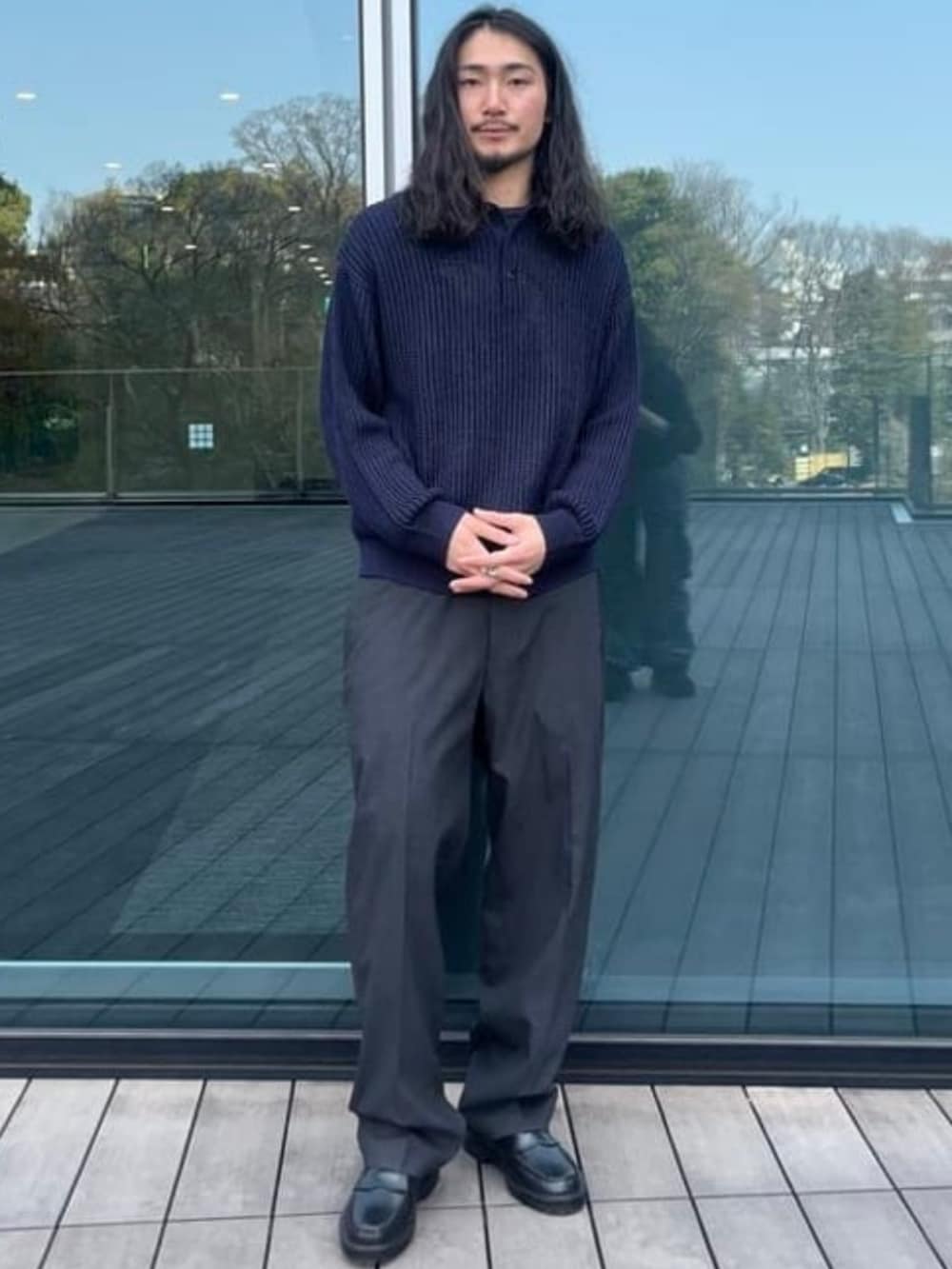 グレー系のスラックス、ブラック系のレインシューズ、ブルー系のニット/セーターを着用したメンズの春コーディネートの2枚目の写真