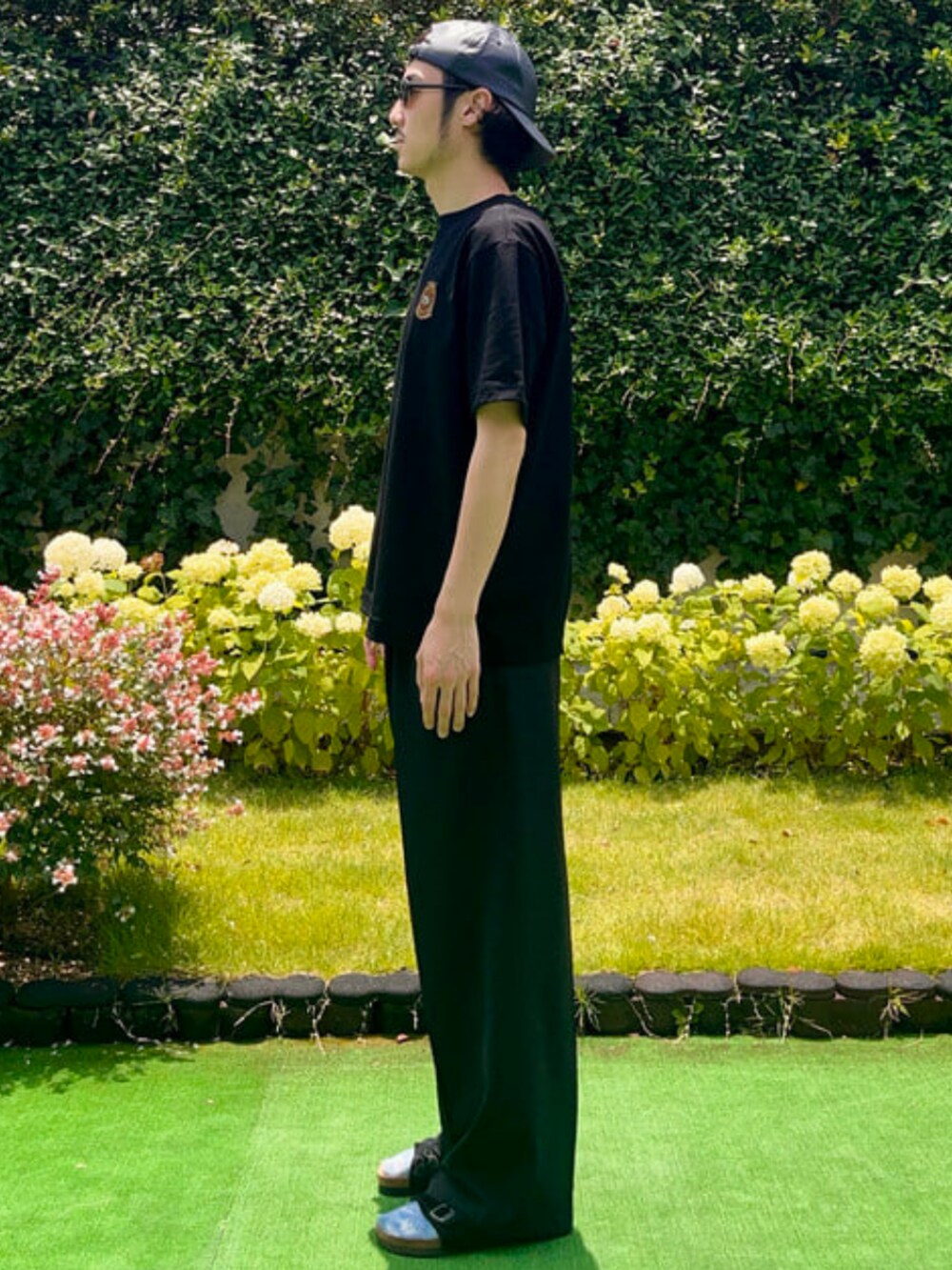 ブラック系のTシャツ/カットソー、ブラック系のサンダル、ブラック系のキャップを着用したメンズの夏コーディネートの2枚目の写真