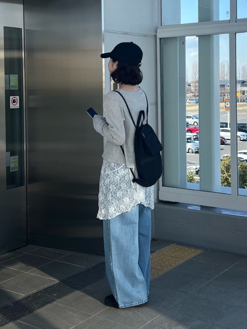 ブルー系のデニムパンツ、グレー系のカーディガン/ボレロ、ブラック系のバックパック/リュックを着用したレディースの春コーディネートの2枚目の写真