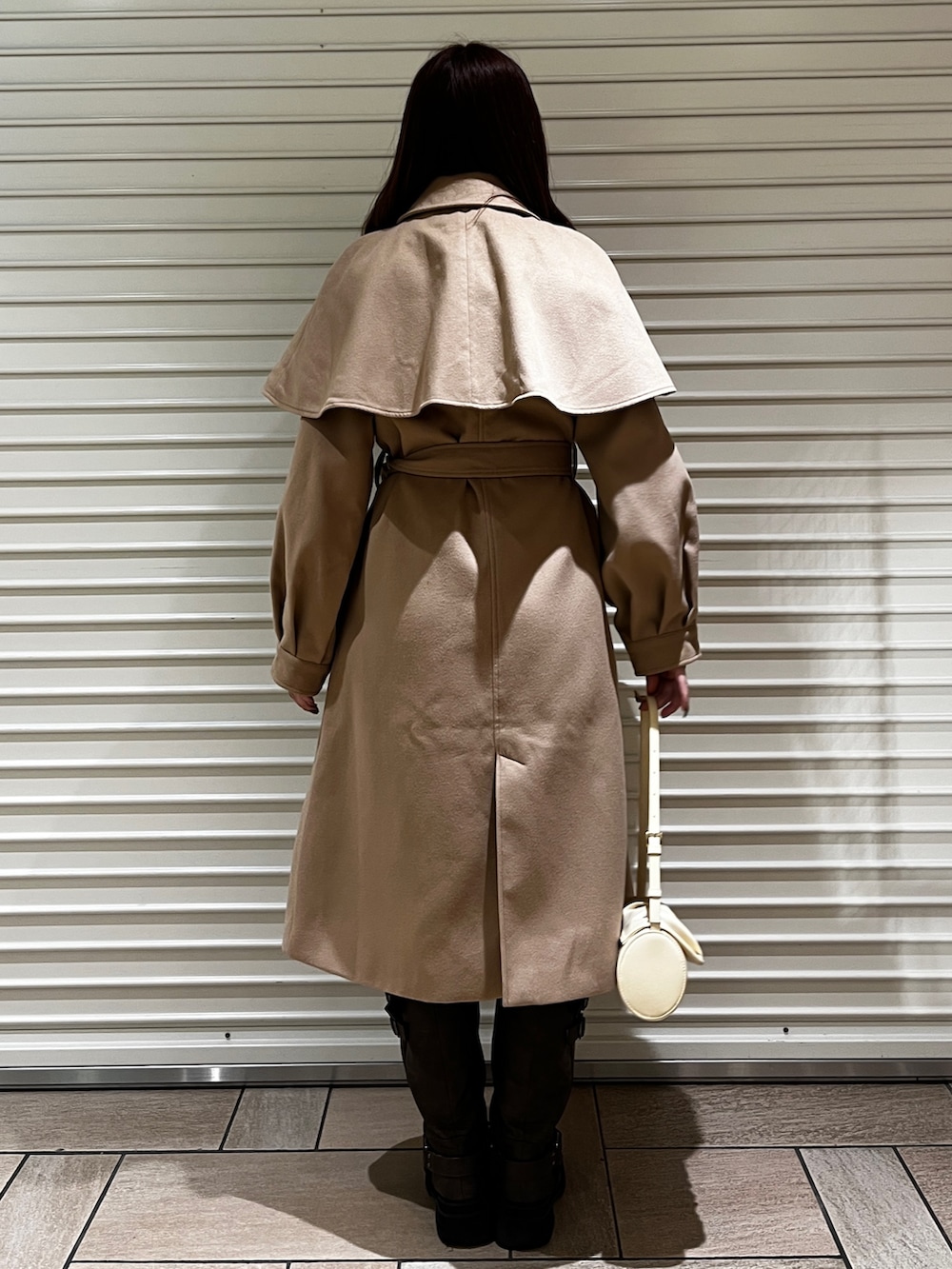 イエロー系のステンカラーコート、ブラウン系のブーツ、イエロー系のハンドバッグを着用したレディースの冬コーディネートの3枚目の写真