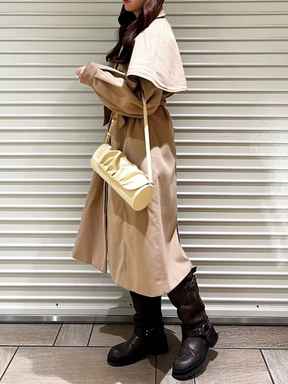 イエロー系のステンカラーコート、ブラウン系のブーツ、イエロー系のハンドバッグを着用したレディースの冬コーディネートの2枚目の写真