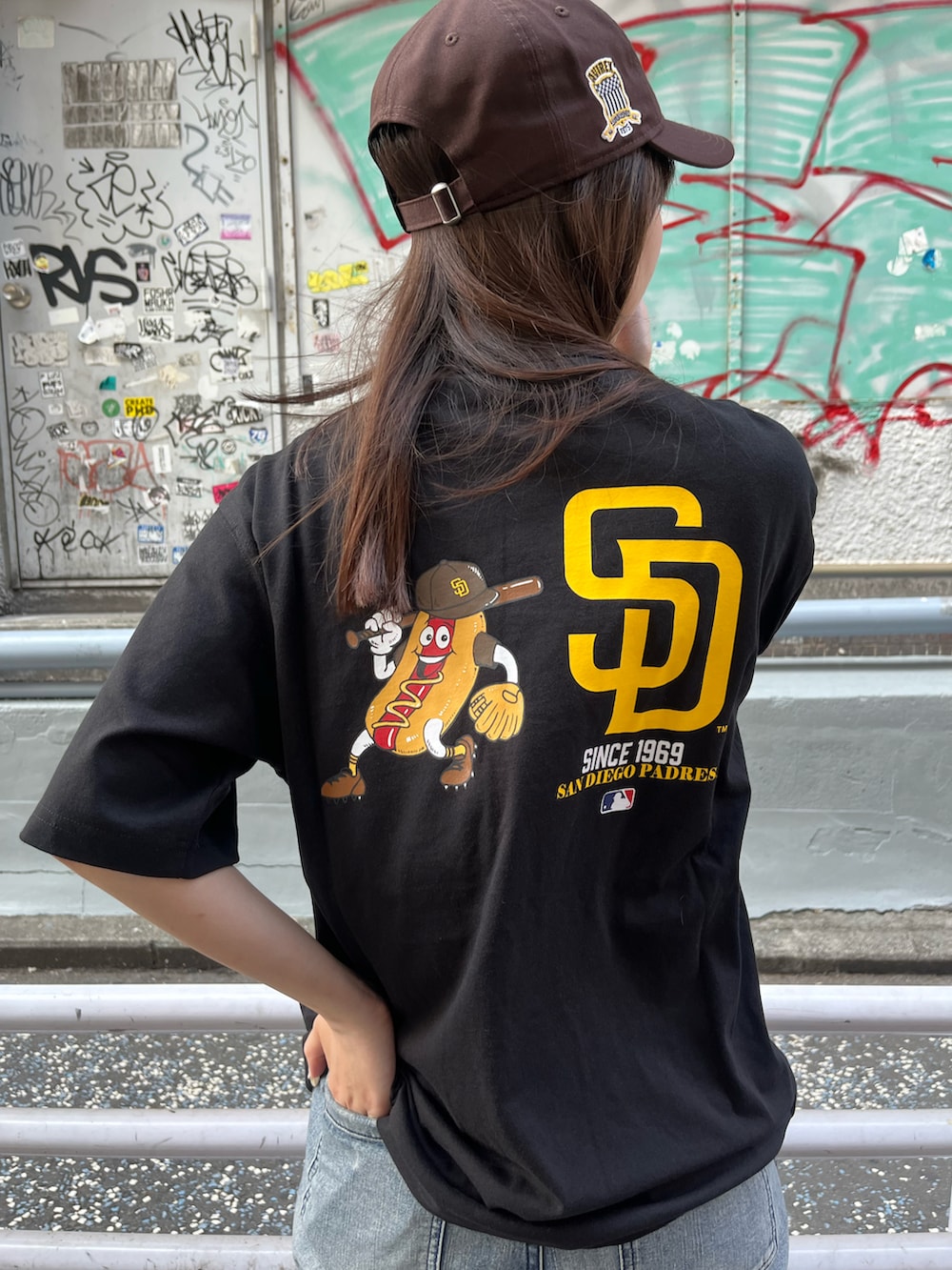ブルー系のデニムパンツ、ブラック系のTシャツ/カットソー、ブラウン系のキャップを着用したレディースの夏コーディネートの3枚目の写真