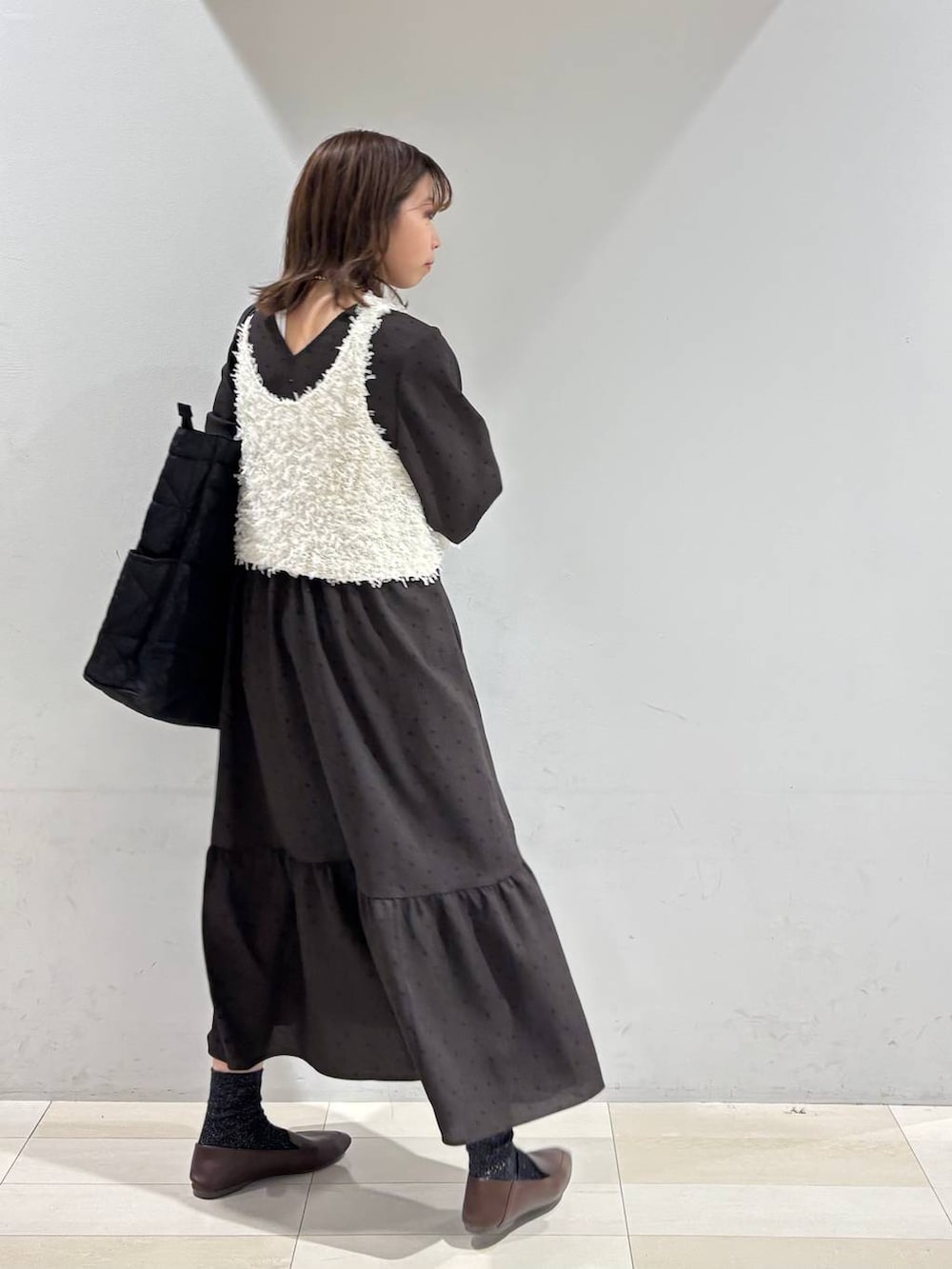 ブラック系のトートバッグ、ブラウン系のワンピース、ホワイト系のベストを着用したレディースの春コーディネートの4枚目の写真