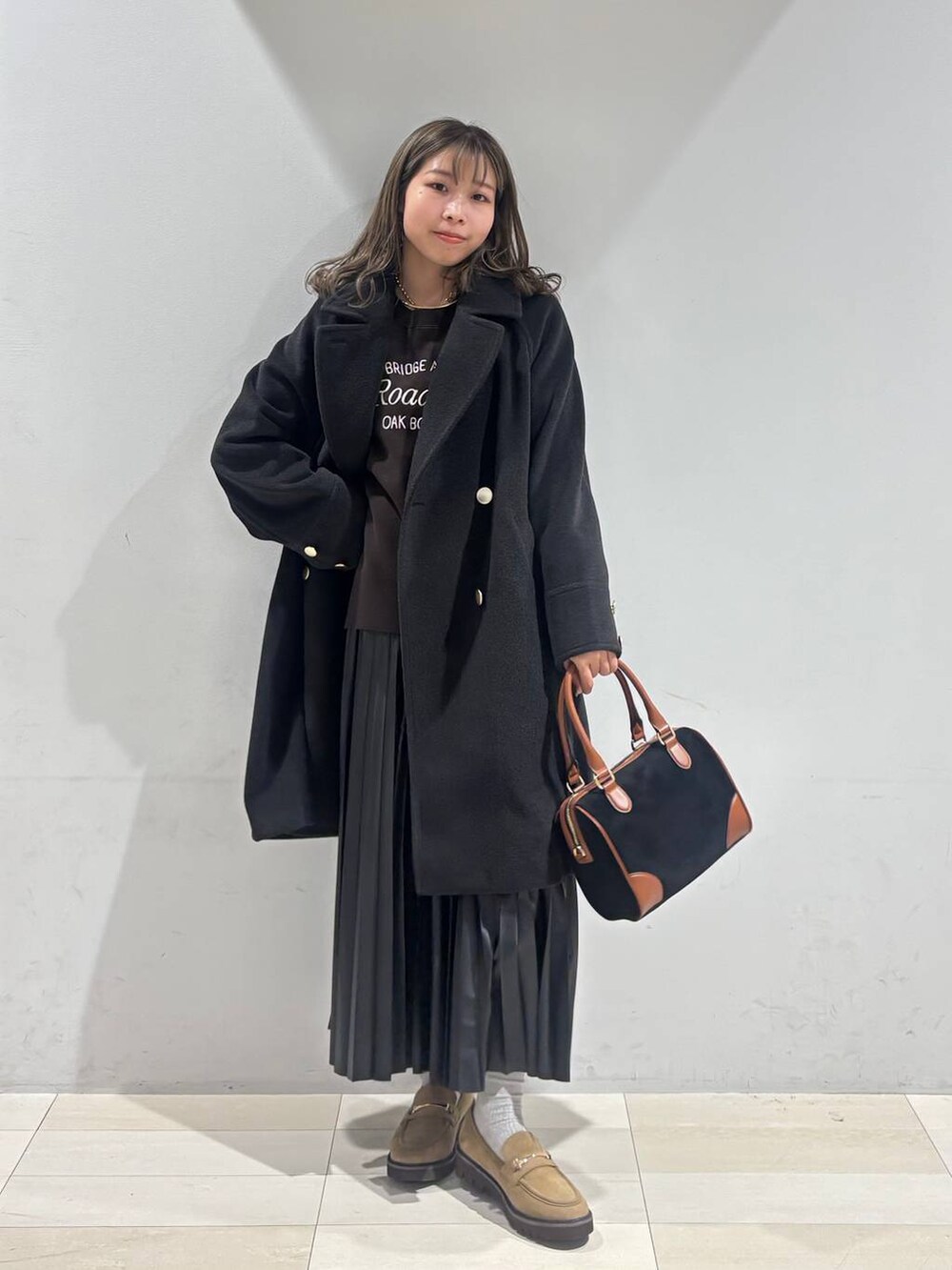 ブラック系のチェスターコート、ベージュ系のローファー、ブラック系のスカートを着用したレディースの秋コーディネートの2枚目の写真