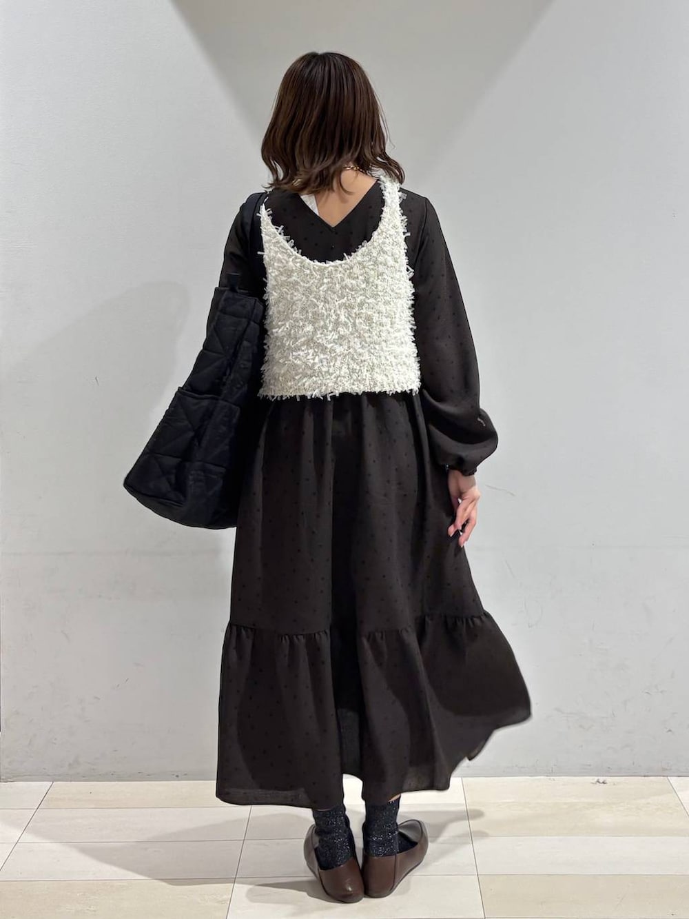 ブラック系のトートバッグ、ブラウン系のワンピース、ホワイト系のベストを着用したレディースの春コーディネートの3枚目の写真