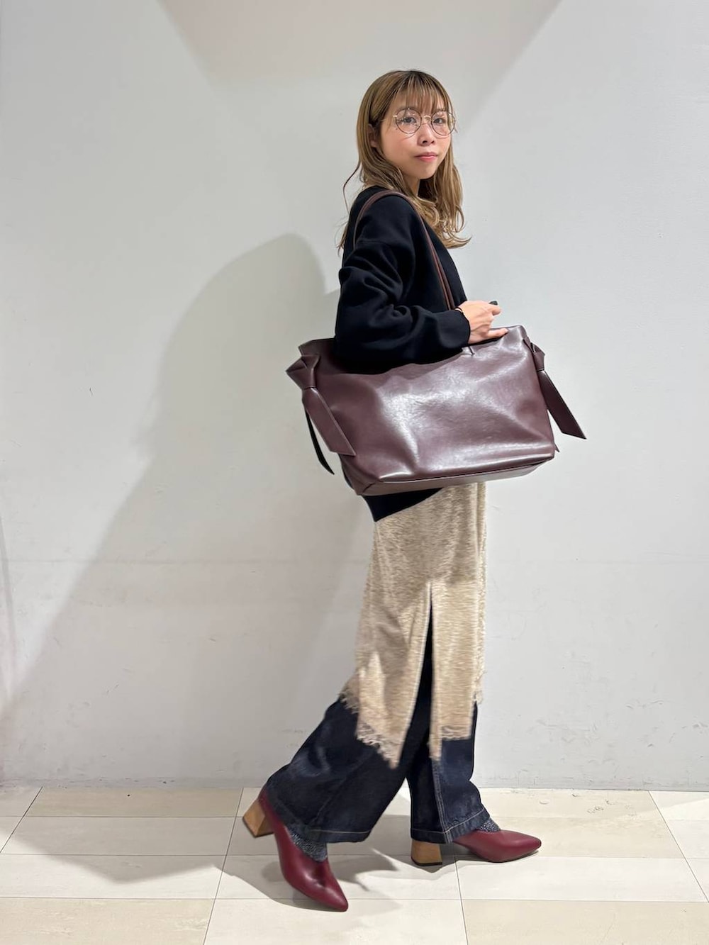 レッド系のトートバッグ、ブラック系のカーディガン/ボレロ、ブルー系のデニムパンツを着用したレディースの秋コーディネートの3枚目の写真