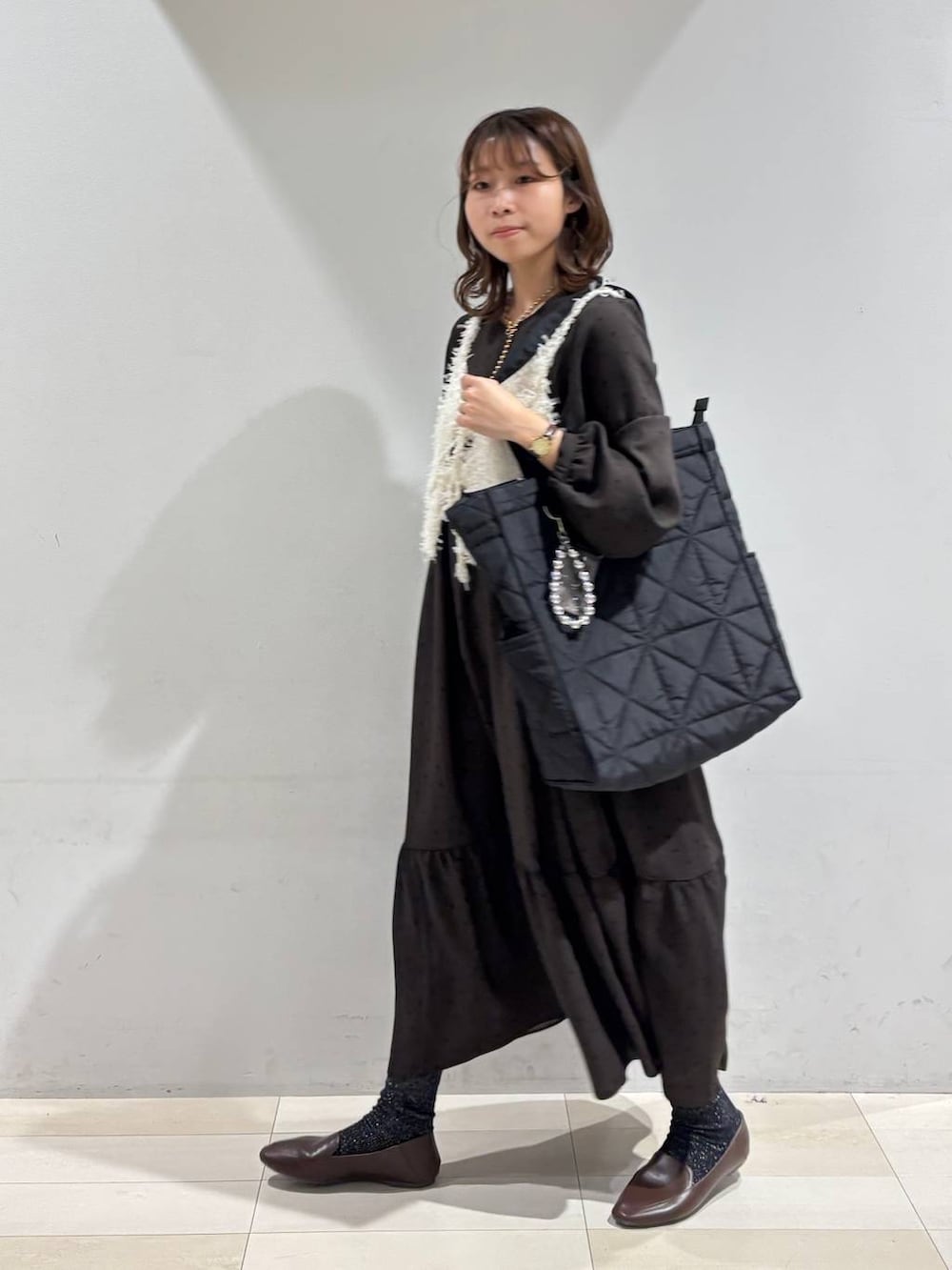 ブラック系のトートバッグ、ブラウン系のワンピース、ホワイト系のベストを着用したレディースの春コーディネートの2枚目の写真