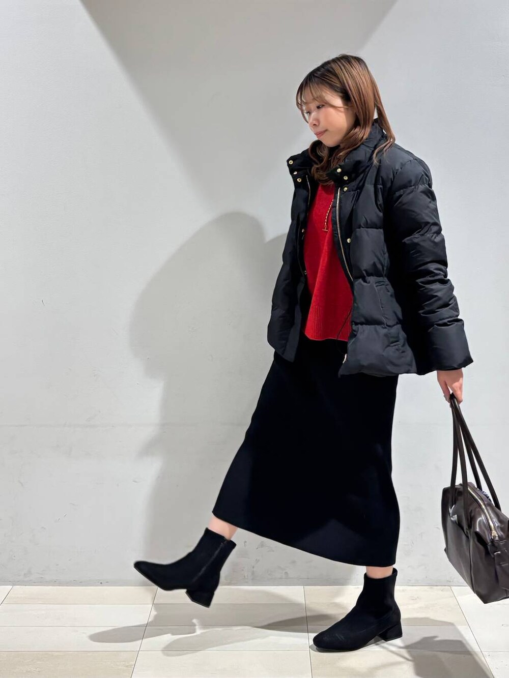 ブラウン系のボストンバッグ、ブラック系のダウンジャケット/コート、ブラック系のスカートを着用したレディースの冬コーディネートの4枚目の写真