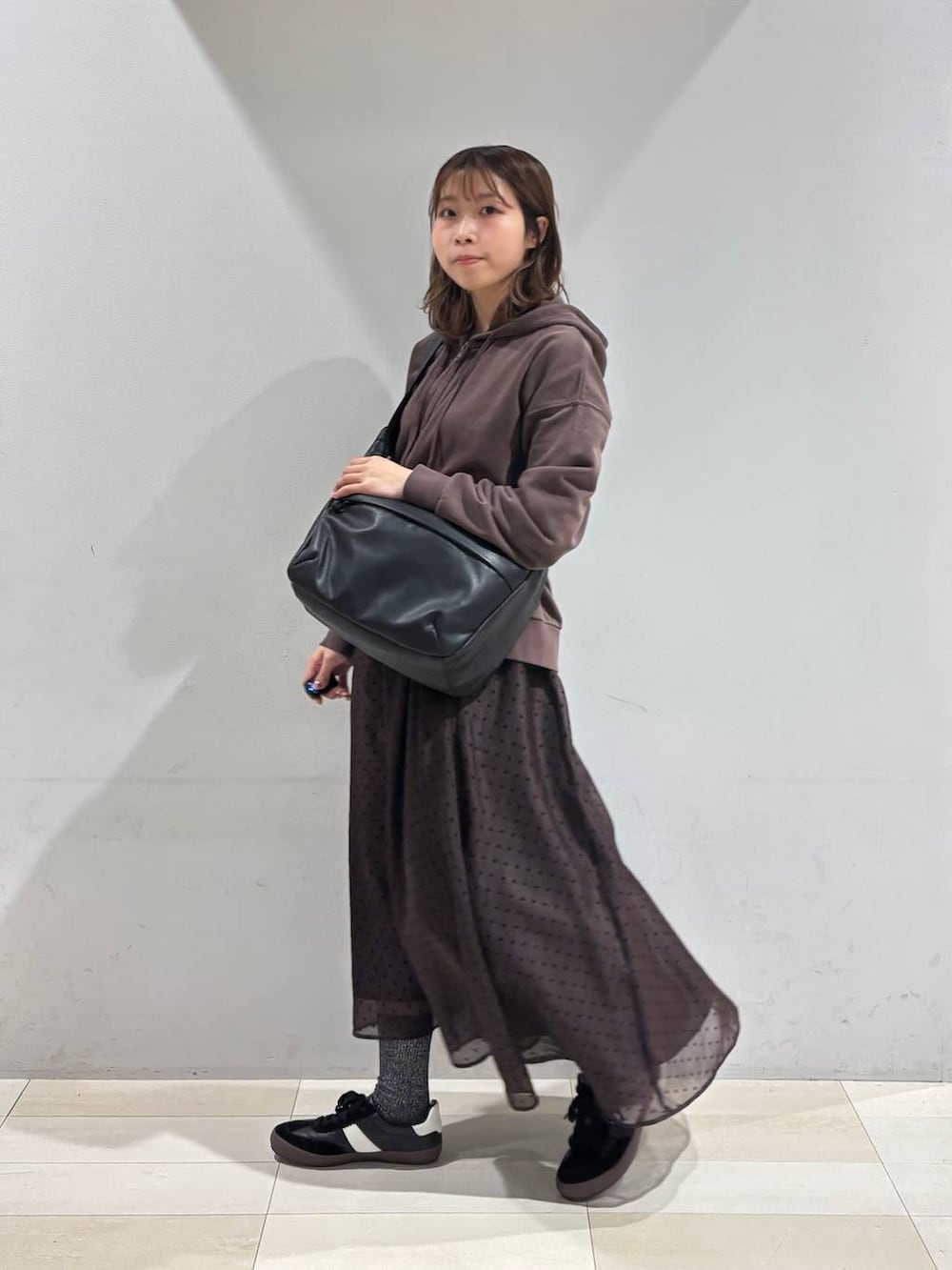 ブラック系のスニーカー、ブラック系のショルダーバッグ、ブラウン系のスカートを着用したレディースの春コーディネートの3枚目の写真