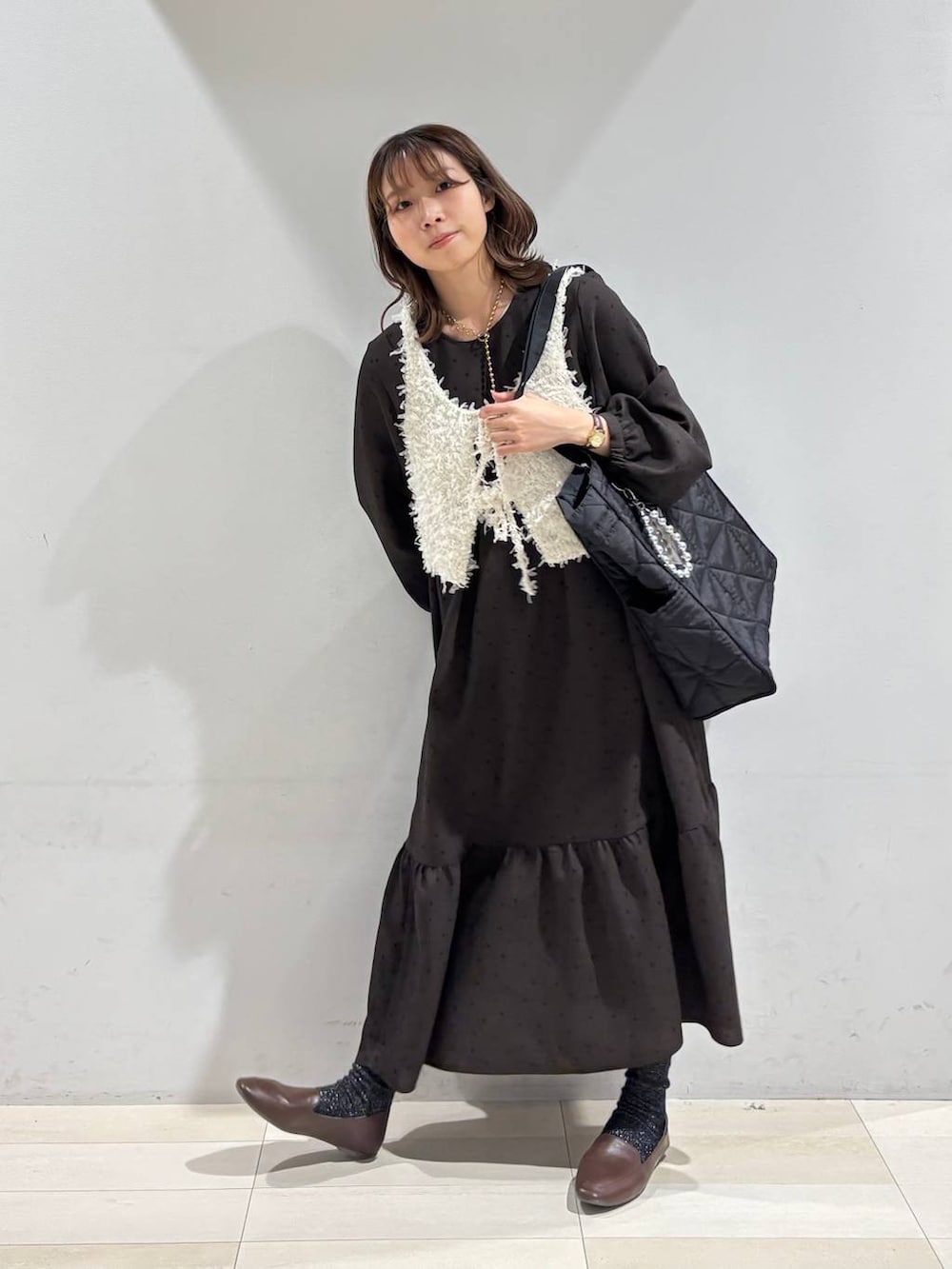 ブラック系のトートバッグ、ブラウン系のワンピース、ホワイト系のベストを着用したレディースの春コーディネートの6枚目の写真