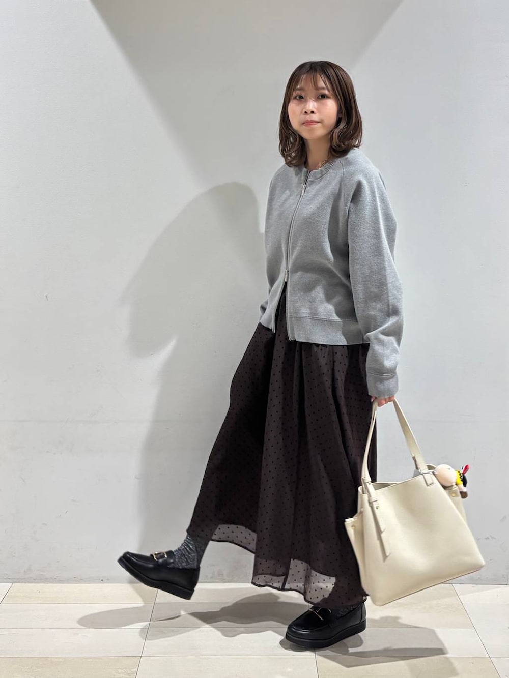 ブラック系のローファー、ホワイト系のハンドバッグ、ブラウン系のスカートを着用したレディースの春コーディネートの2枚目の写真